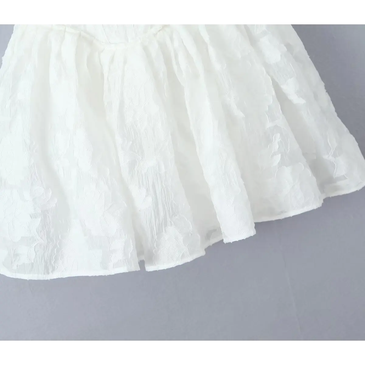 Close-up of the flared skirt hem with floral jacquard texture on the white dress