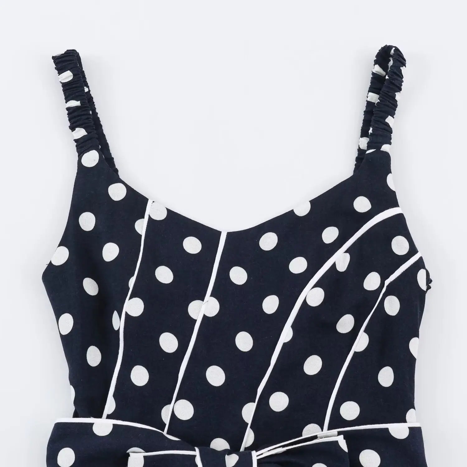 Close‑up of v‑neck bodice, contrast white piping, navy fabric with white polka dot print, smocked strap attachment