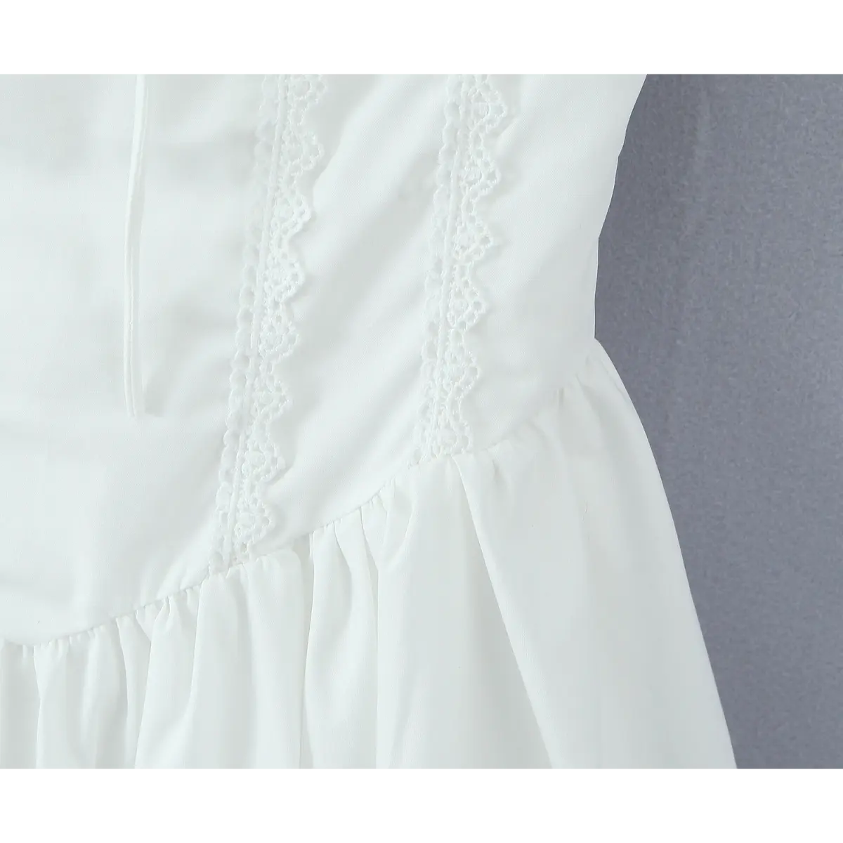 Close-up of the waistline seam and vertical lace trim on the white dress bodice
