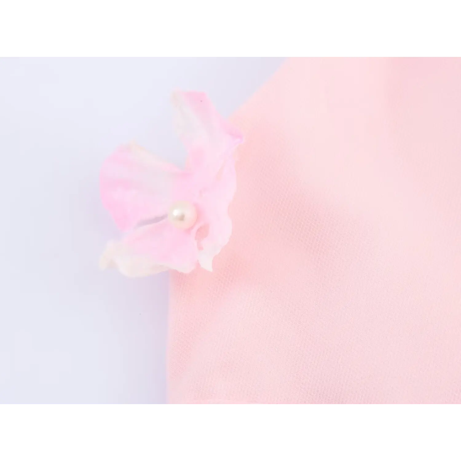 Macro shot of handmade gradient pink organza flower with central faux pearl, attached to pink halter slip dress mesh fabric, romantic floral decoration detail