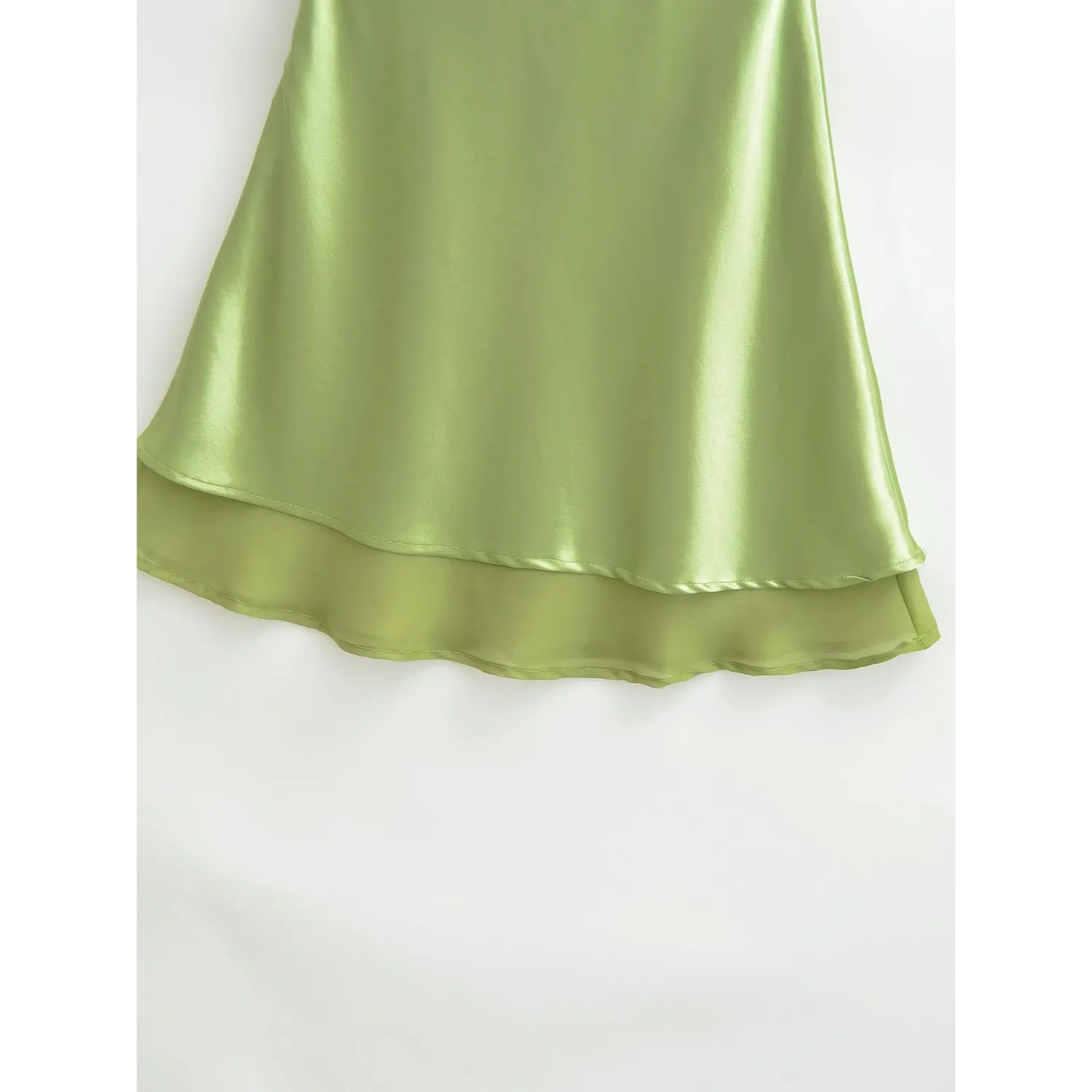Close-up of avocado green satin skirt double-layer hem, showing glossy satin outer fabric and lightweight chiffon lining