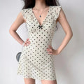Model wearing beige black polka dot mini dress with ruffle V-neck and bow detail, retro feminine outfit