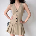 Model wearing beige vest-style mini dress with black button detailing and pleated hem