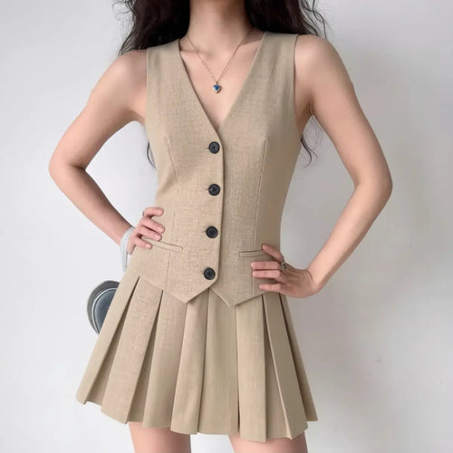Model wearing beige vest-style mini dress with black button detailing and pleated hem