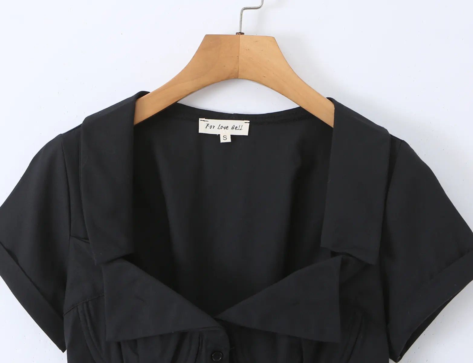 Black corset-style short-sleeve shirt hanging on wooden hanger, full front view