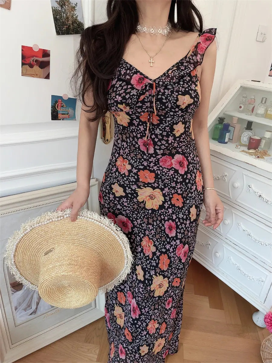 Model wearing black floral cami maxi dress with ruffled straps, V-neckline and front tie detail
