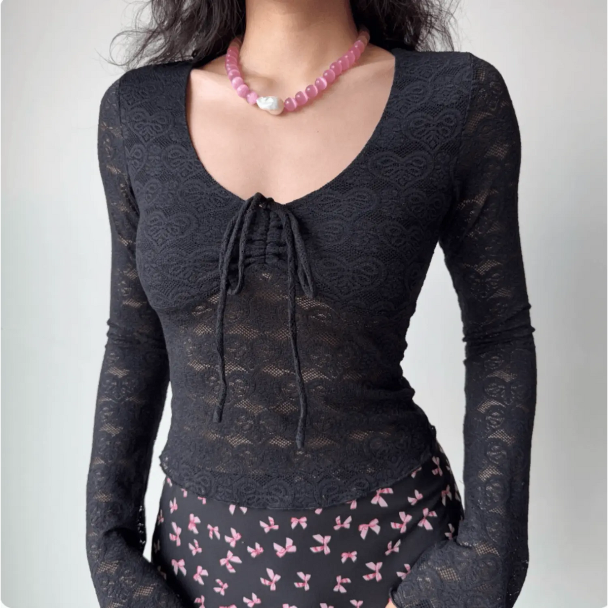 Model wearing black semi‑sheer lace long sleeve top with front drawstring ruched v‑neck