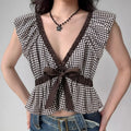 Model wearing black white gingham top with V-neck, ruffled trim and bow accent, flowy peplum blouse