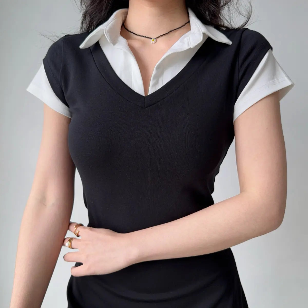 Model wearing black preppy-style faux two-piece dress with V-neck, white shirt collar, and short sleeves