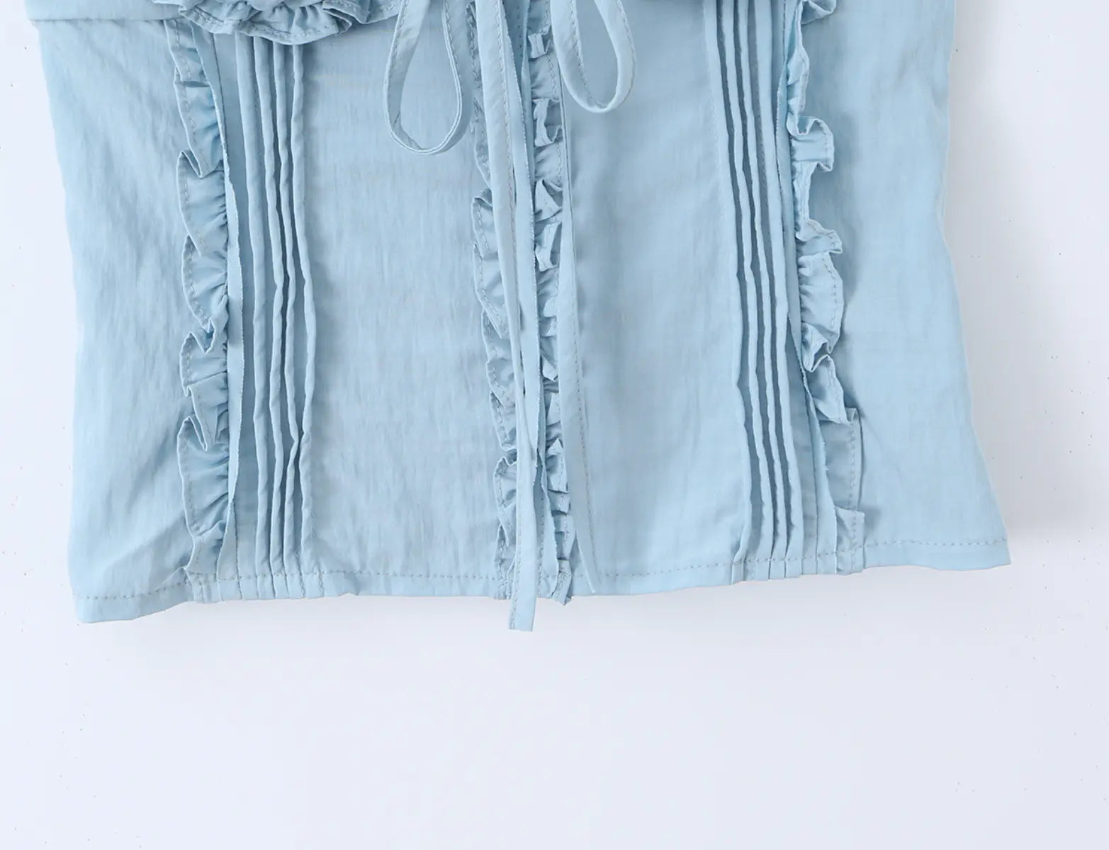 Close-up of the vertical pleats, ruffled trim and fabric texture on the light blue cami top