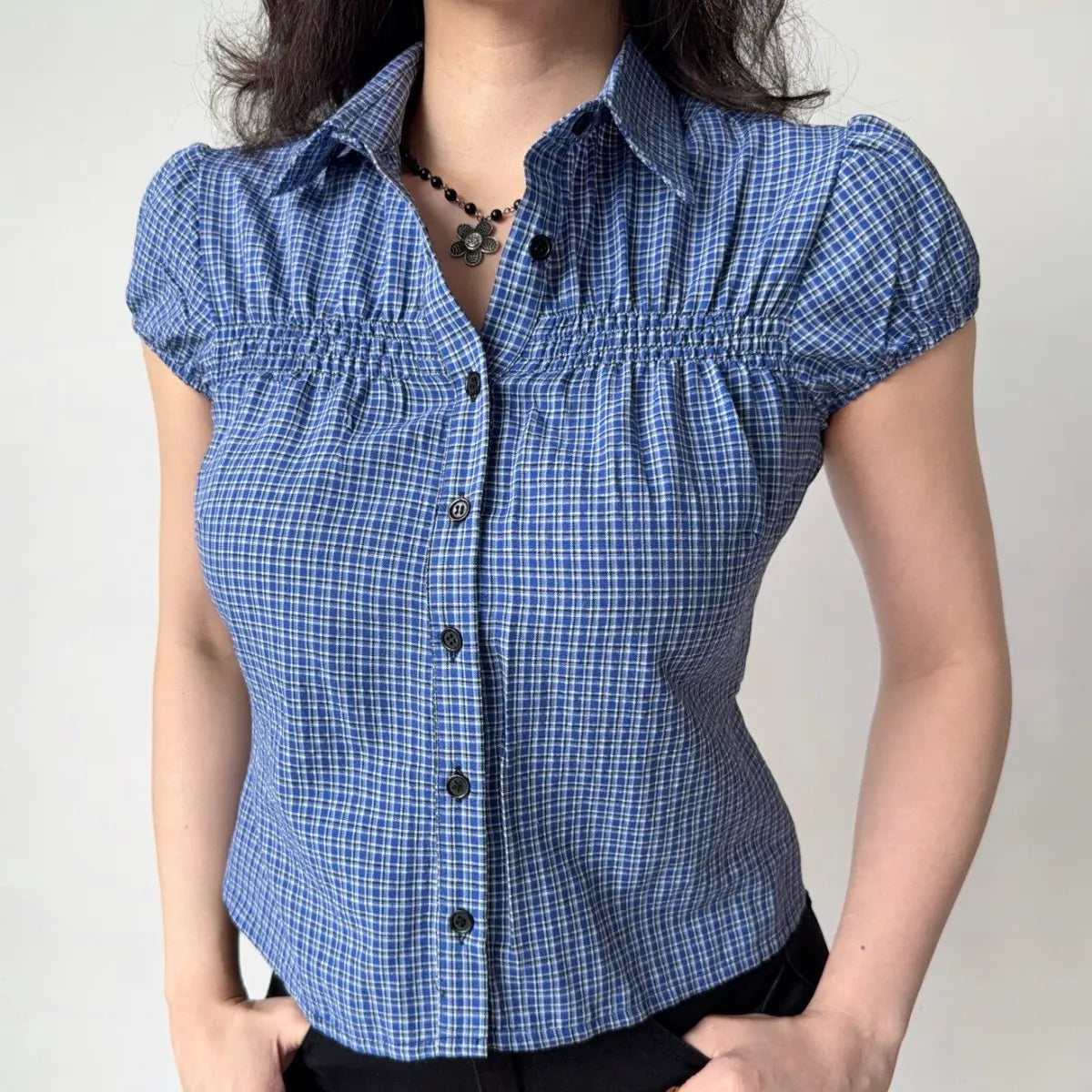 Model wearing blue gingham checkered shirt with puffed short sleeves, button-down front, and smocked bust detailing