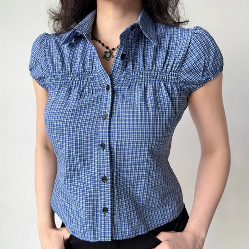 Model wearing blue gingham checkered shirt with puffed short sleeves, button-down front, and smocked bust detailing