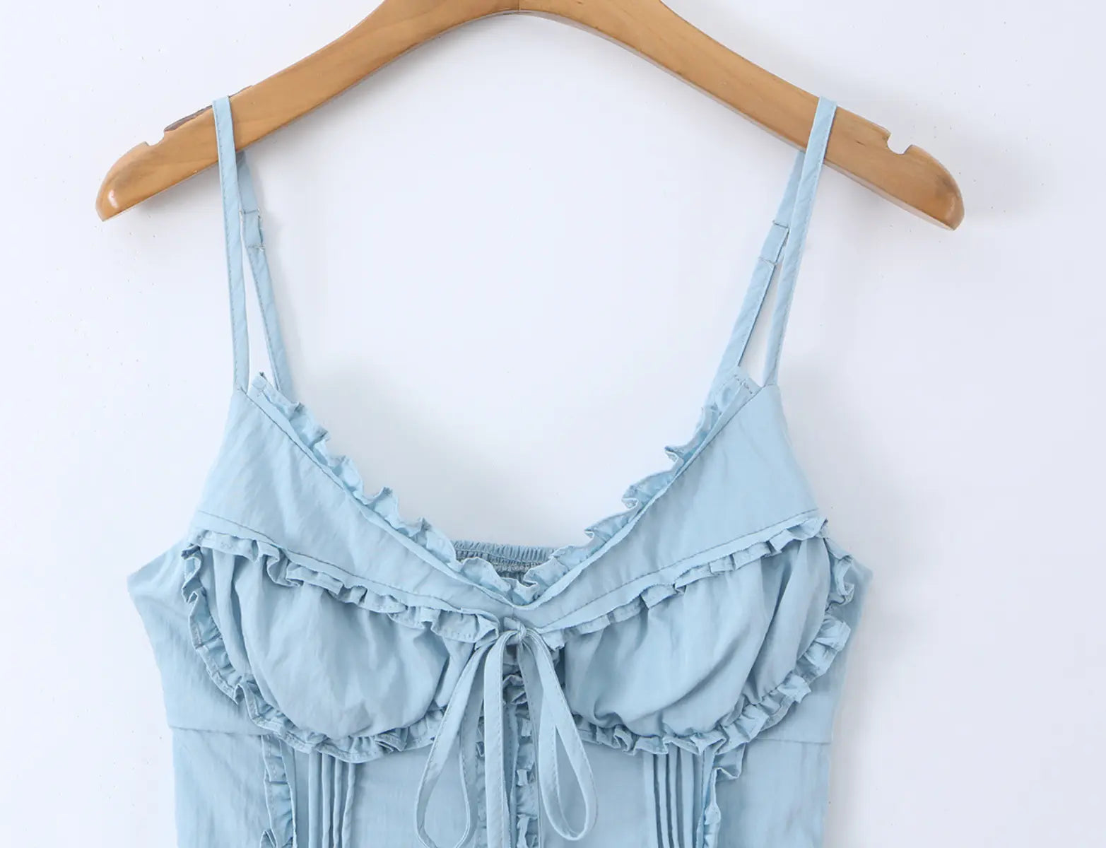 Light blue ruffled cami top hanging on wooden hanger, full front view