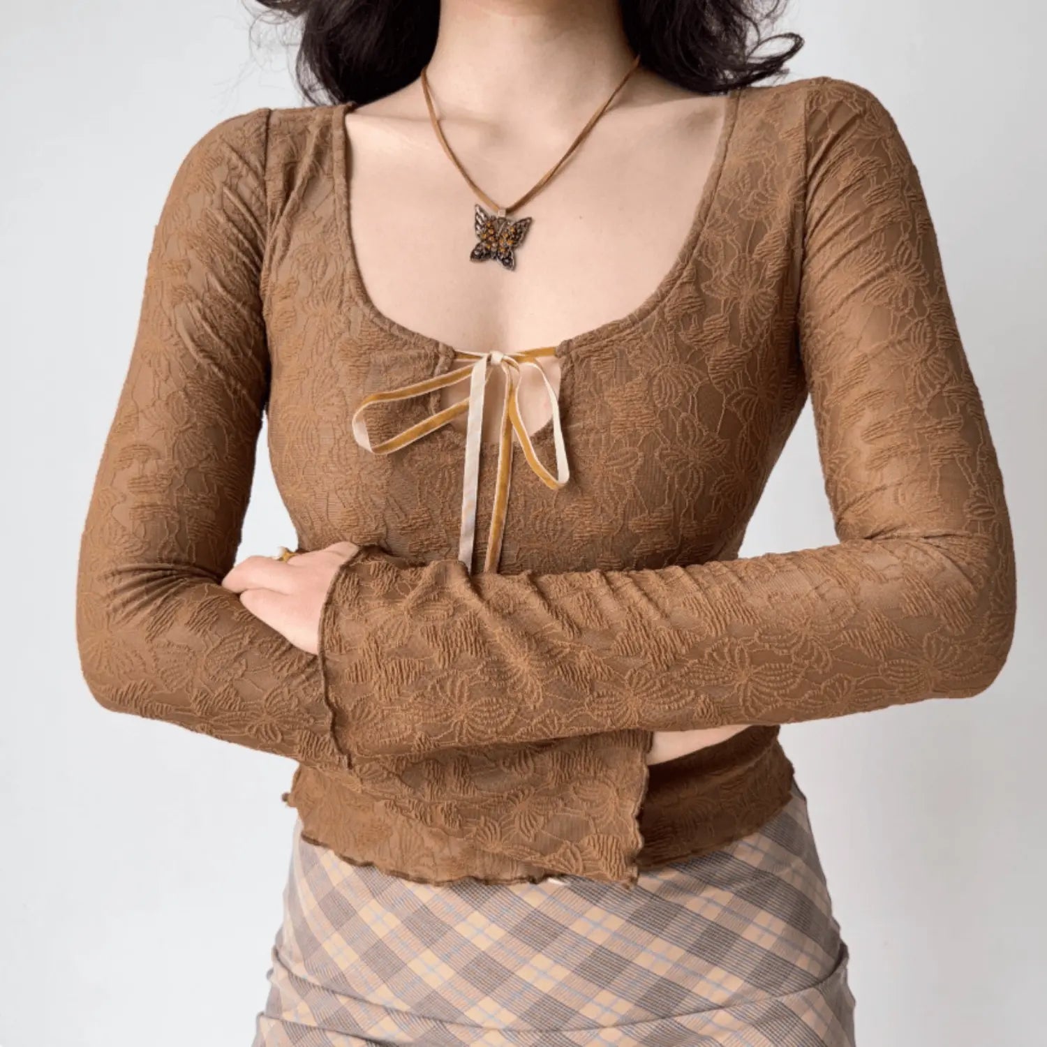 Model wearing brown floral lace long sleeve top with front ribbon tie, crossed‑arms pose