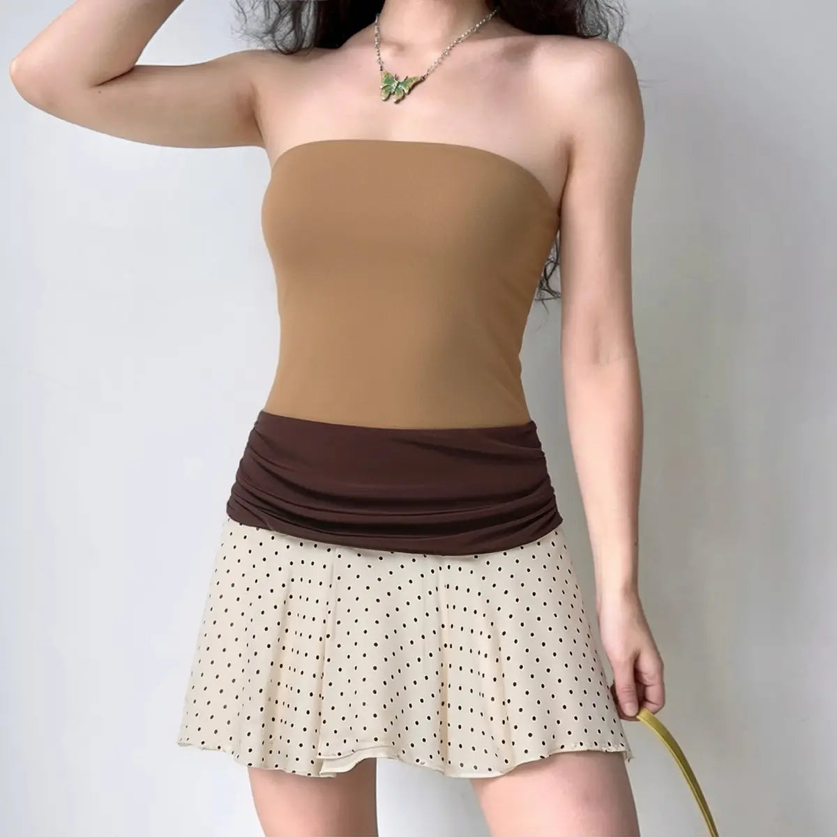 Model wearing camel two-tone bandeau dress with ruched waist detail and polka dot skirt hem, form-fitting strapless mini dress