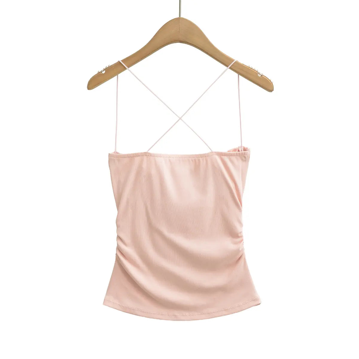Cami top on a wooden hanger, showing crisscross straps, ruched sides and smooth knit fabric.