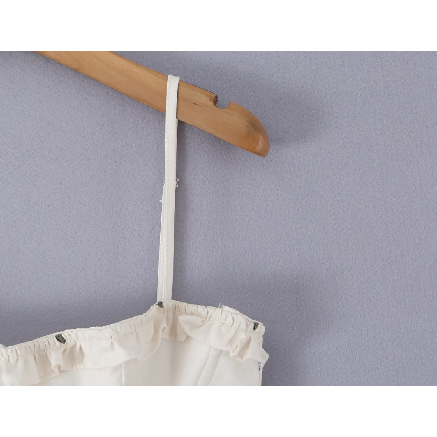 Macro detail of thin adjustable spaghetti strap with metal slider buckle, matching cream fabric piping