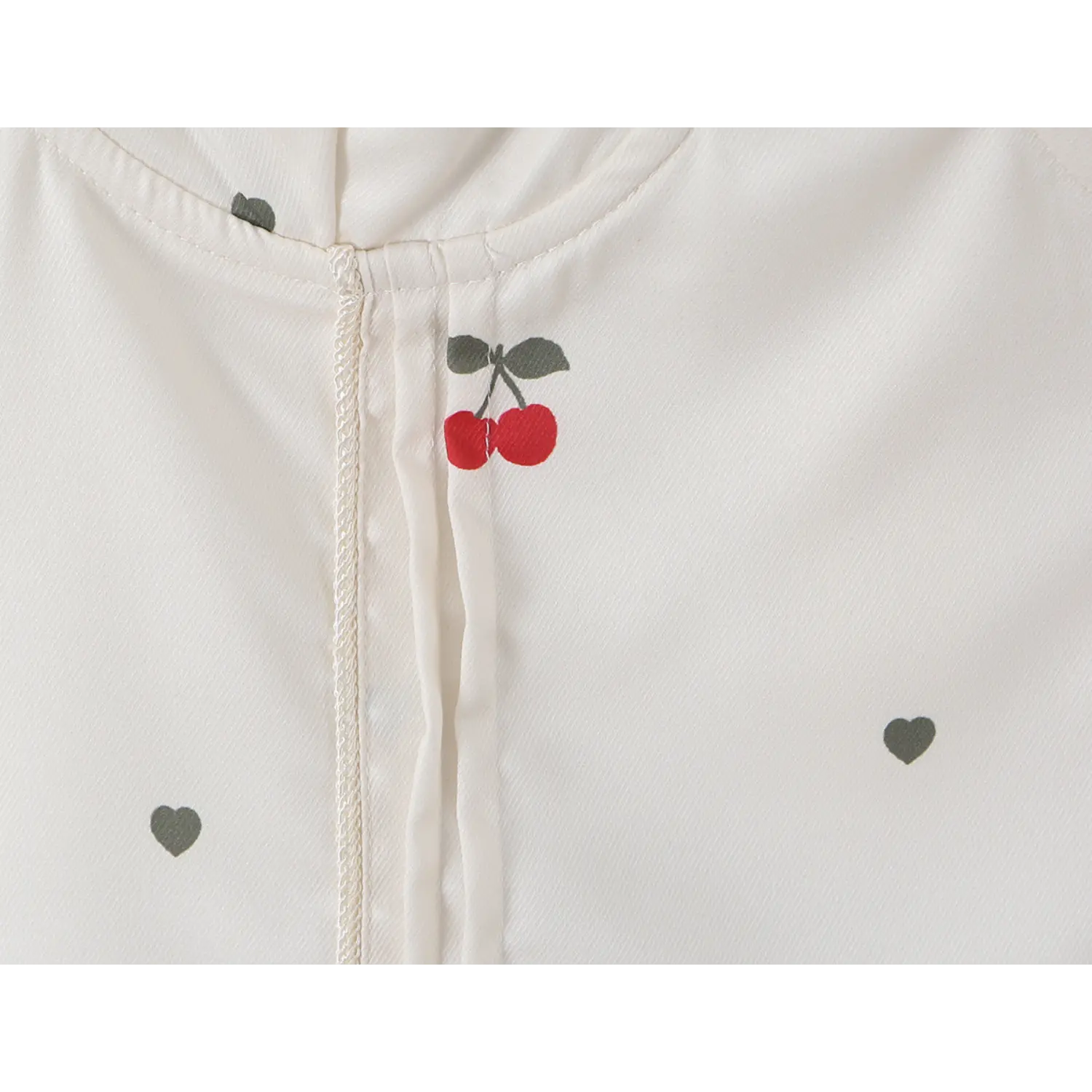 Macro shot of red cherry graphic print and decorative braided center front seam on cream cami top