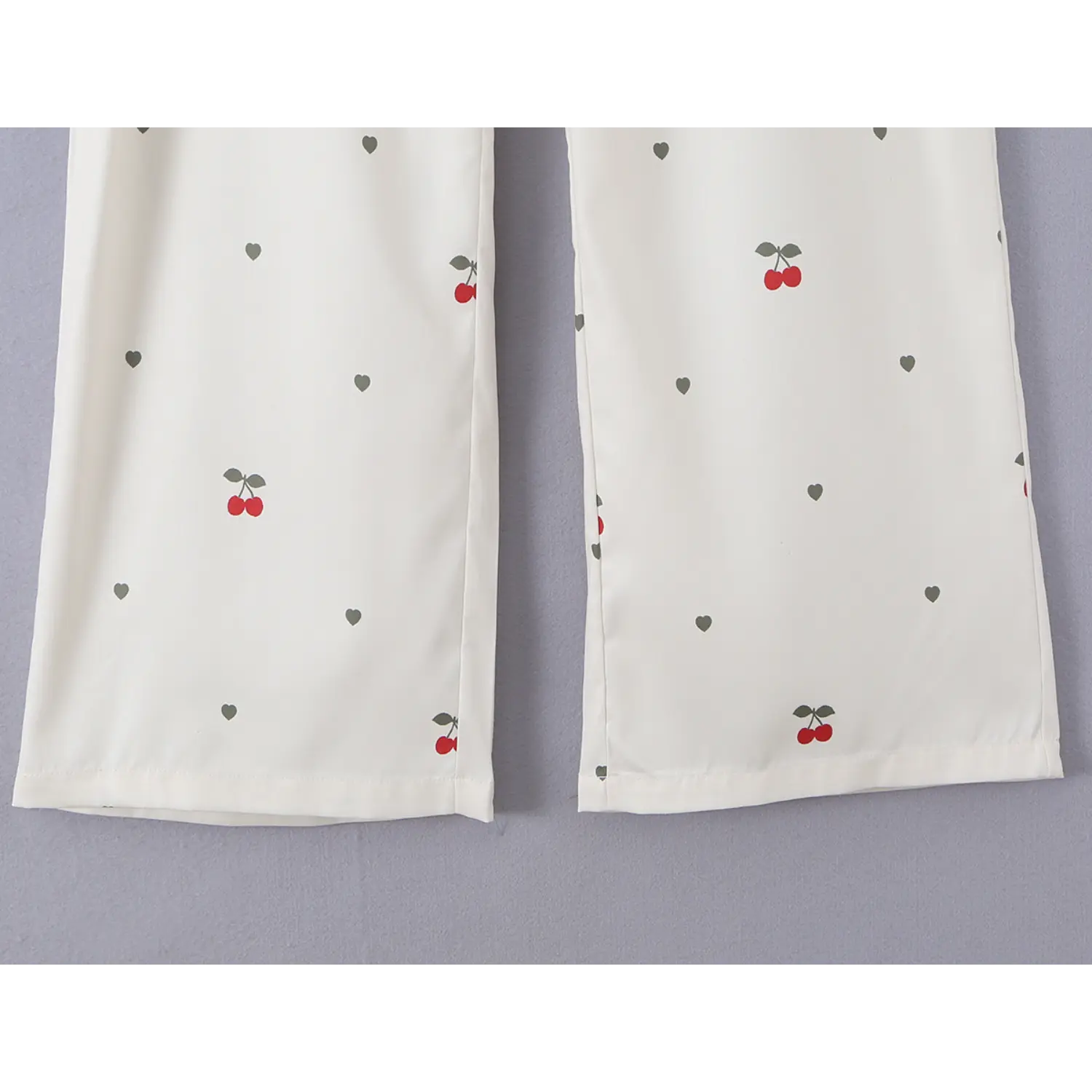 Close-up of pant leg bottom hem with double neat stitching, scattered cherry and mini heart print on cream woven fabric