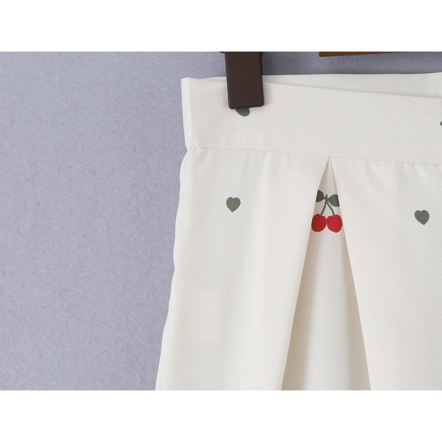 Side waist pleat close-up, showing red cherry and grey heart print on lightweight woven fabric