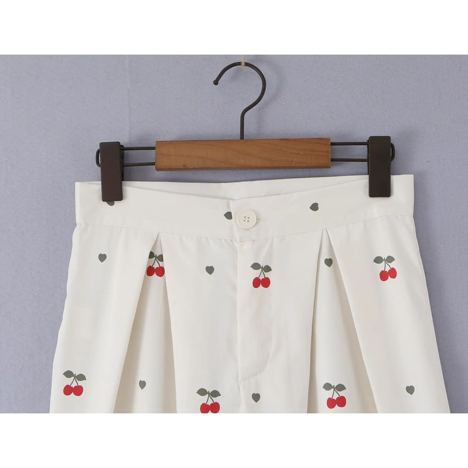 Close-up of front waistband, four-hole button and double front pleats on cream cherry print trousers