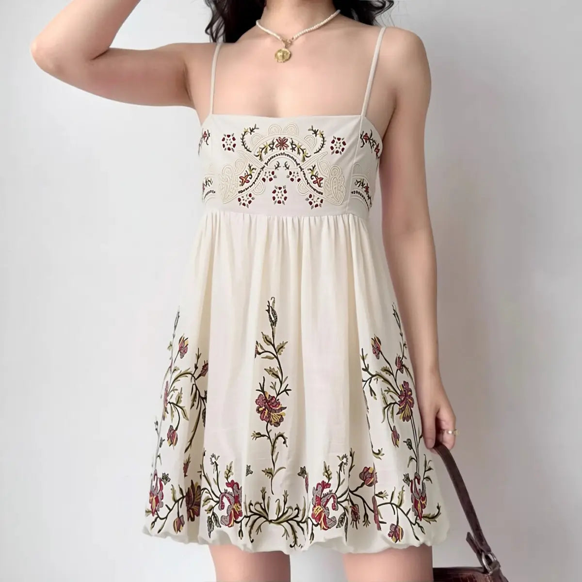 Model wearing cream floral embroidered cami mini dress with spaghetti straps and smocked bust