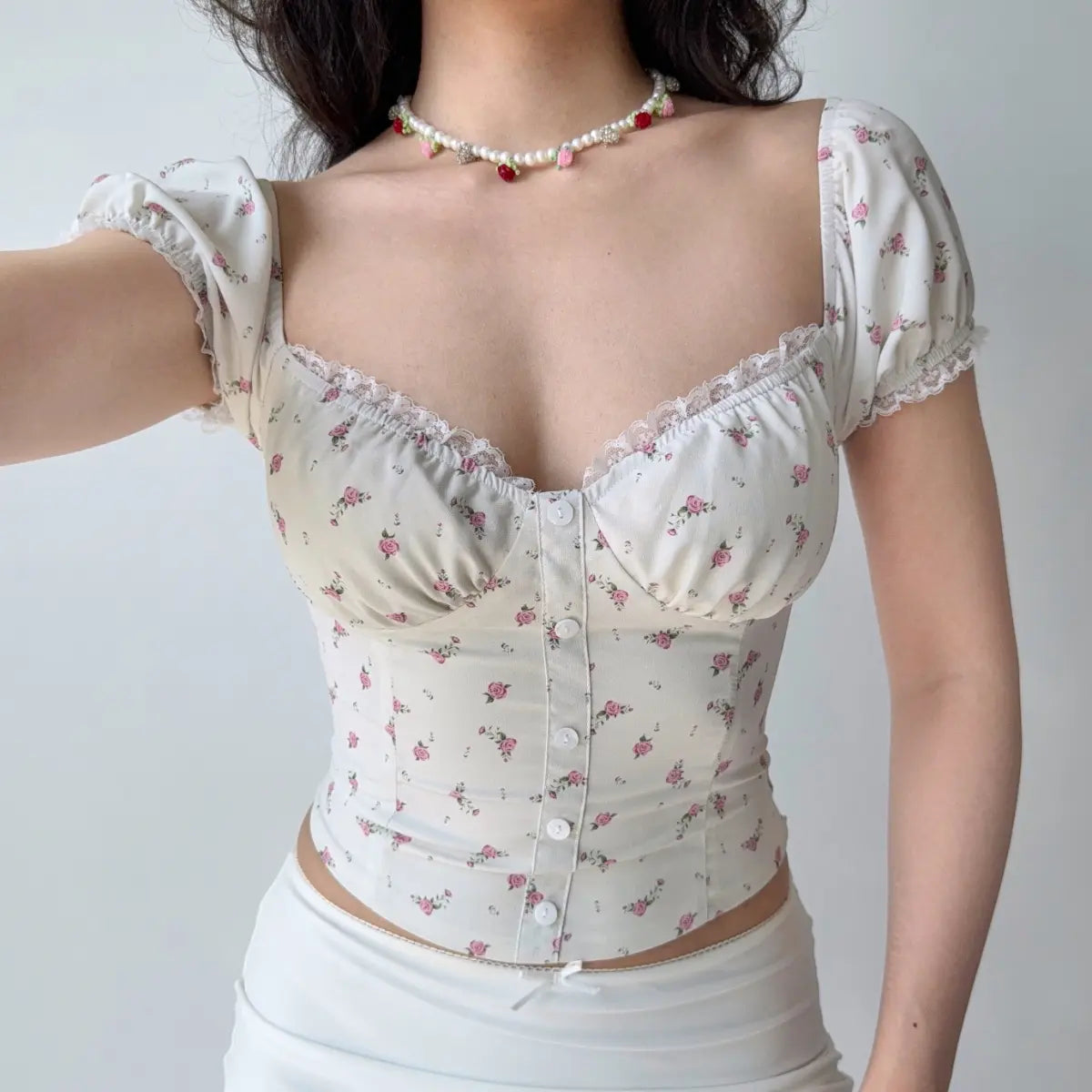 Model wearing cream floral print corset-style top with puff short sleeves, sweetheart neckline, lace trim, and front button placket