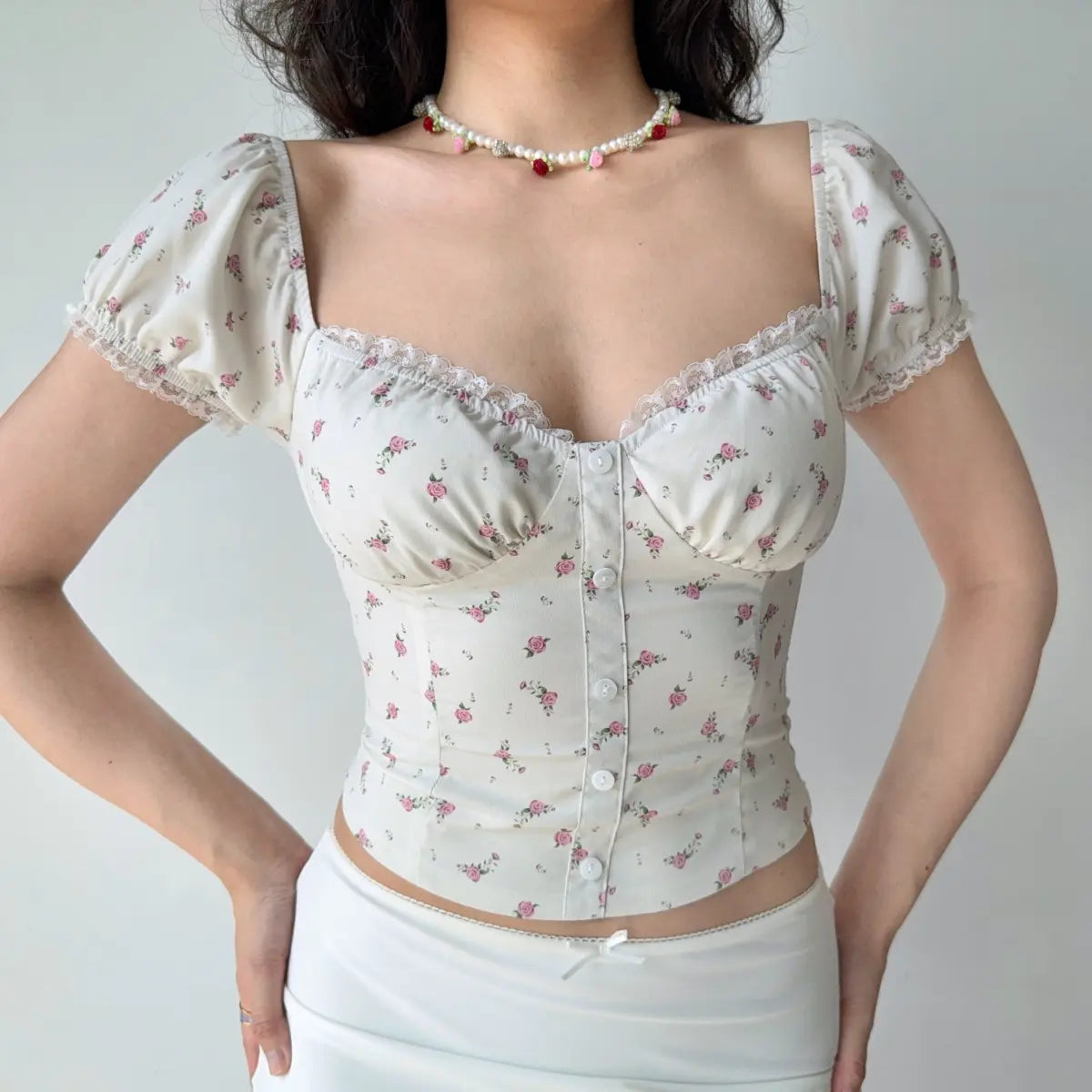 Outfit view of cream floral print top styled with white bottoms, highlighting the cropped, fitted design