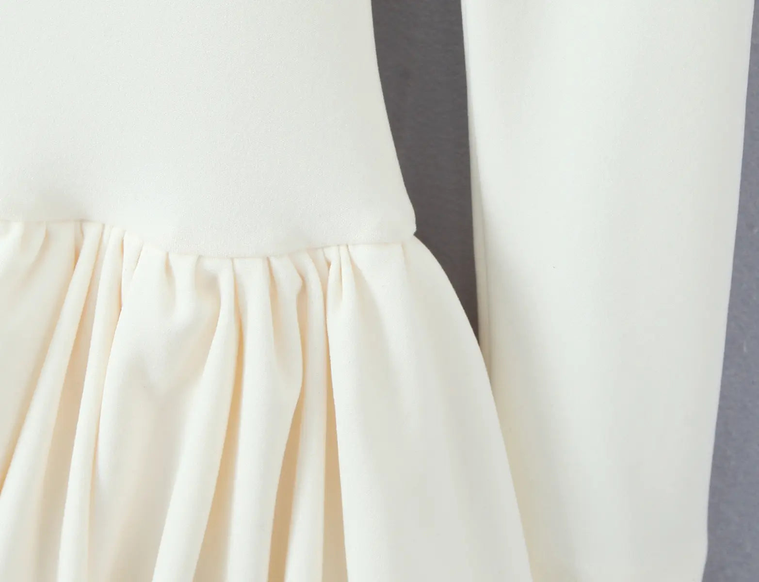 Close-up of gathered ruffled hem on cream-white long-sleeve dress