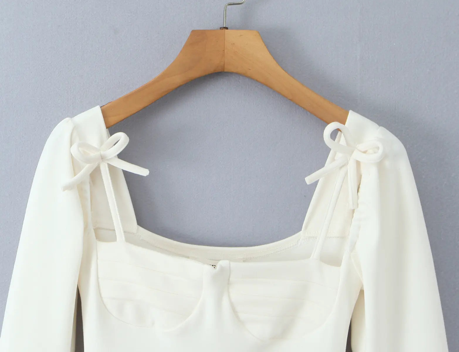 Close-up of square neckline and shoulder bow detail on cream-white dress