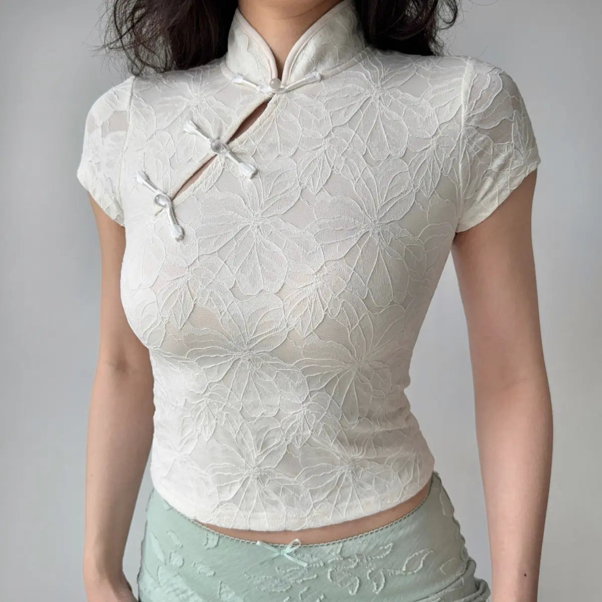 Model wearing cream white embossed qipao-style top with mandarin collar, frog closures and form-fitting silhouette