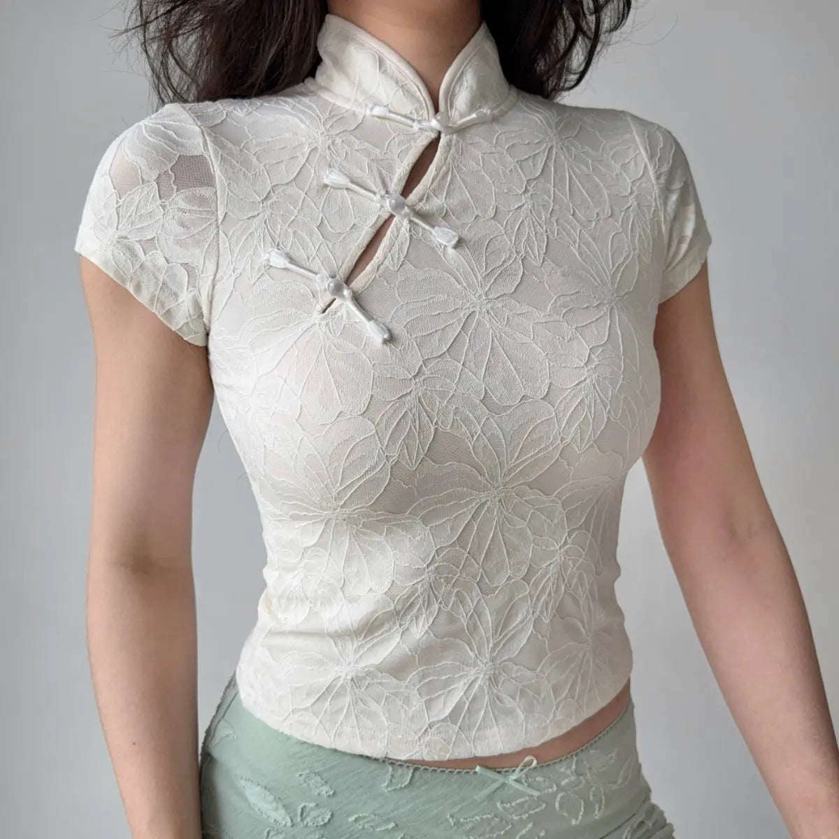 Front view of cream white qipao-style top with traditional frog closures and floral embossed fabric