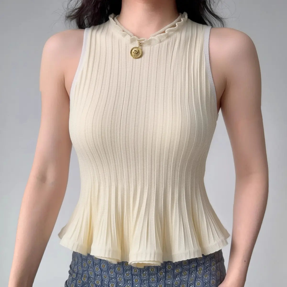 Model wearing cream white ribbed-knit tank with ruffled neckline and peplum hem, fitted sleeveless sweater