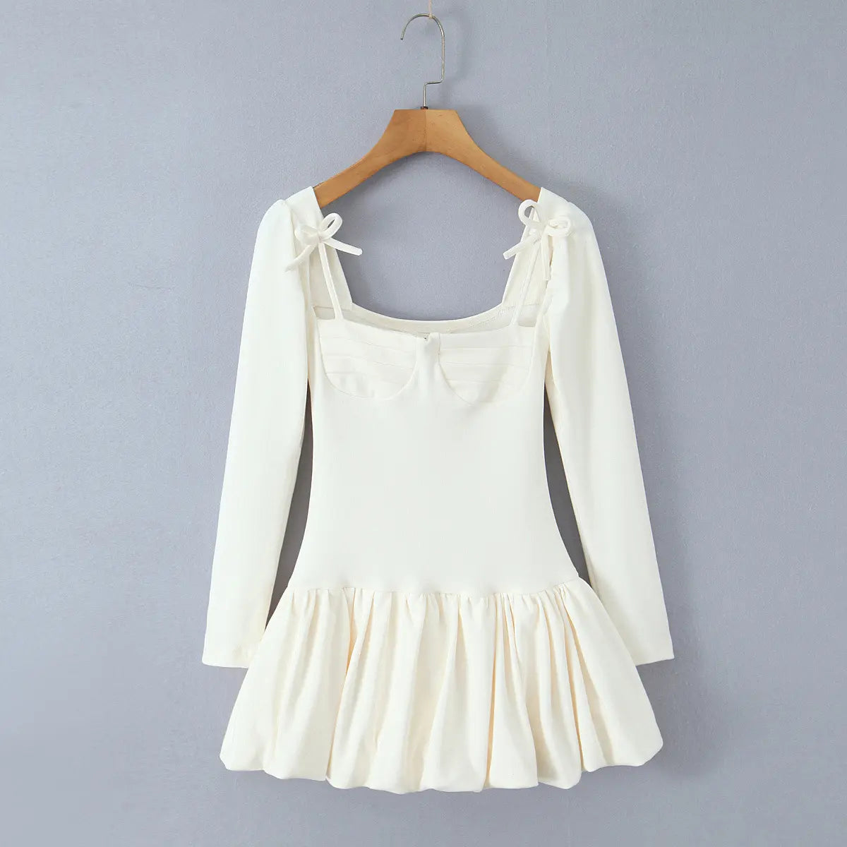 Cream-white long-sleeve dress hanging on wooden hanger, front view