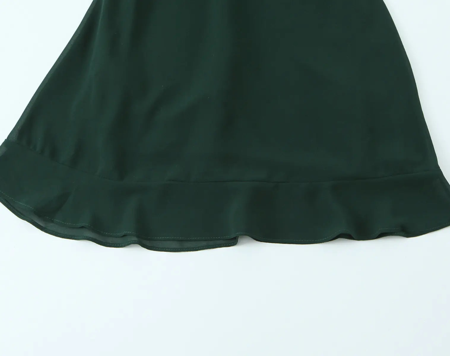 Ruffled hem detail view of dark green cami mini dress on white background