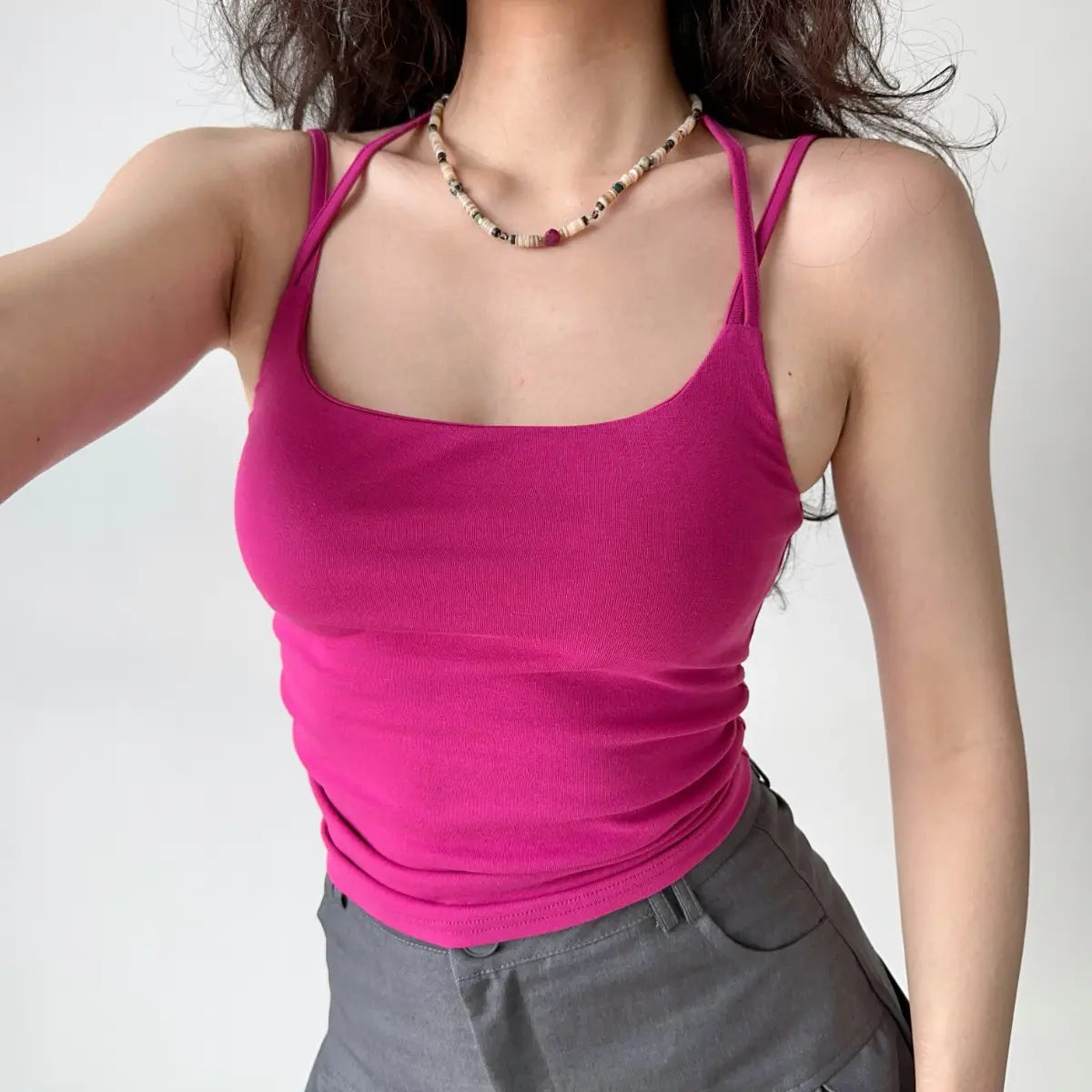 Model wearing fuchsia halter-style cami top with dual shoulder straps, square neckline, and form-fitting cropped silhouette