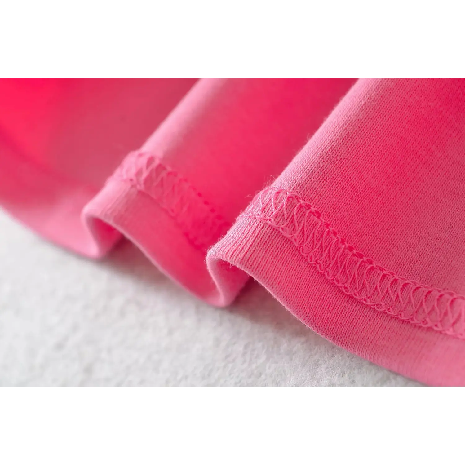 Close-up of serged stitching on short sleeve cuff of hot pink ribbed slim fit U-neck t-shirt, showing neat stretch sewing craft