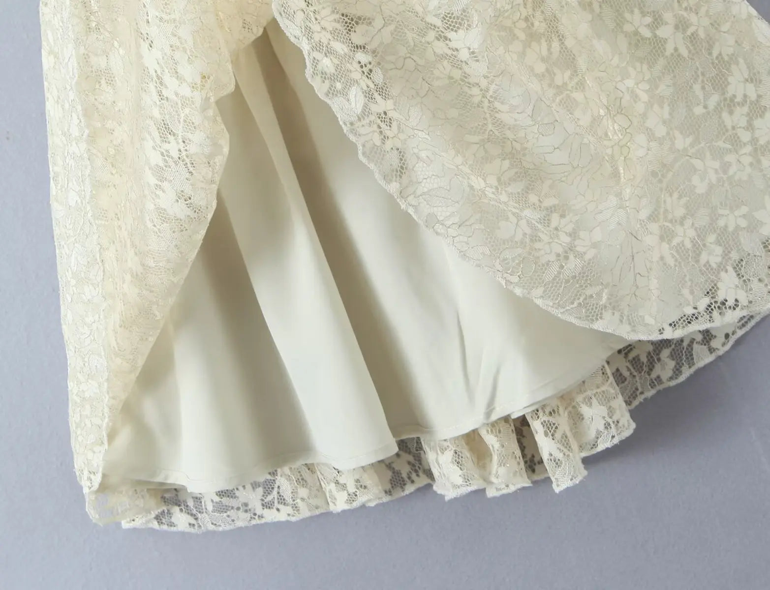Close-up of layered lace hem and lining on ivory cami mini dress