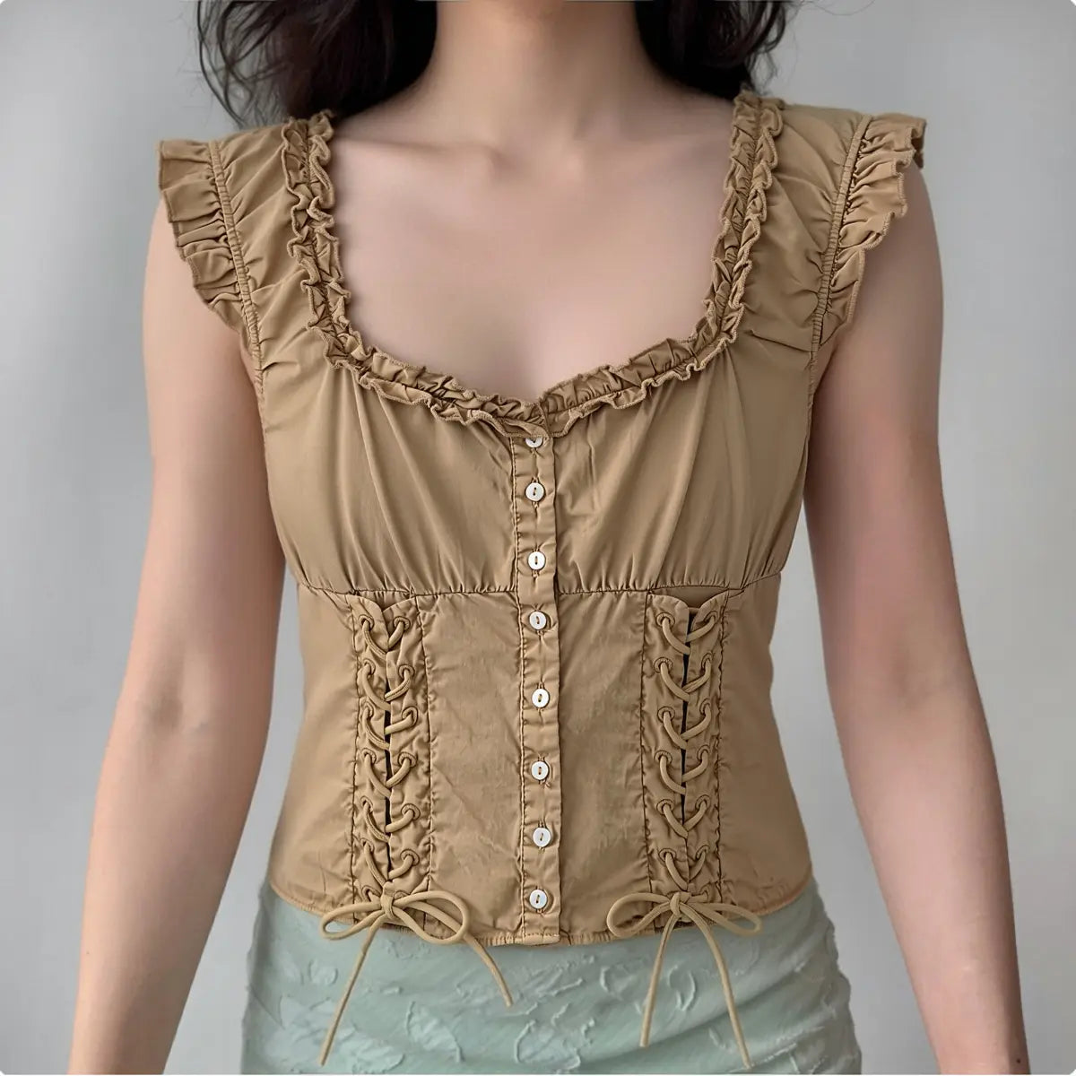 Model wearing khaki corset-style sleeveless top with ruffled trim, lace-up details and fitted silhouette