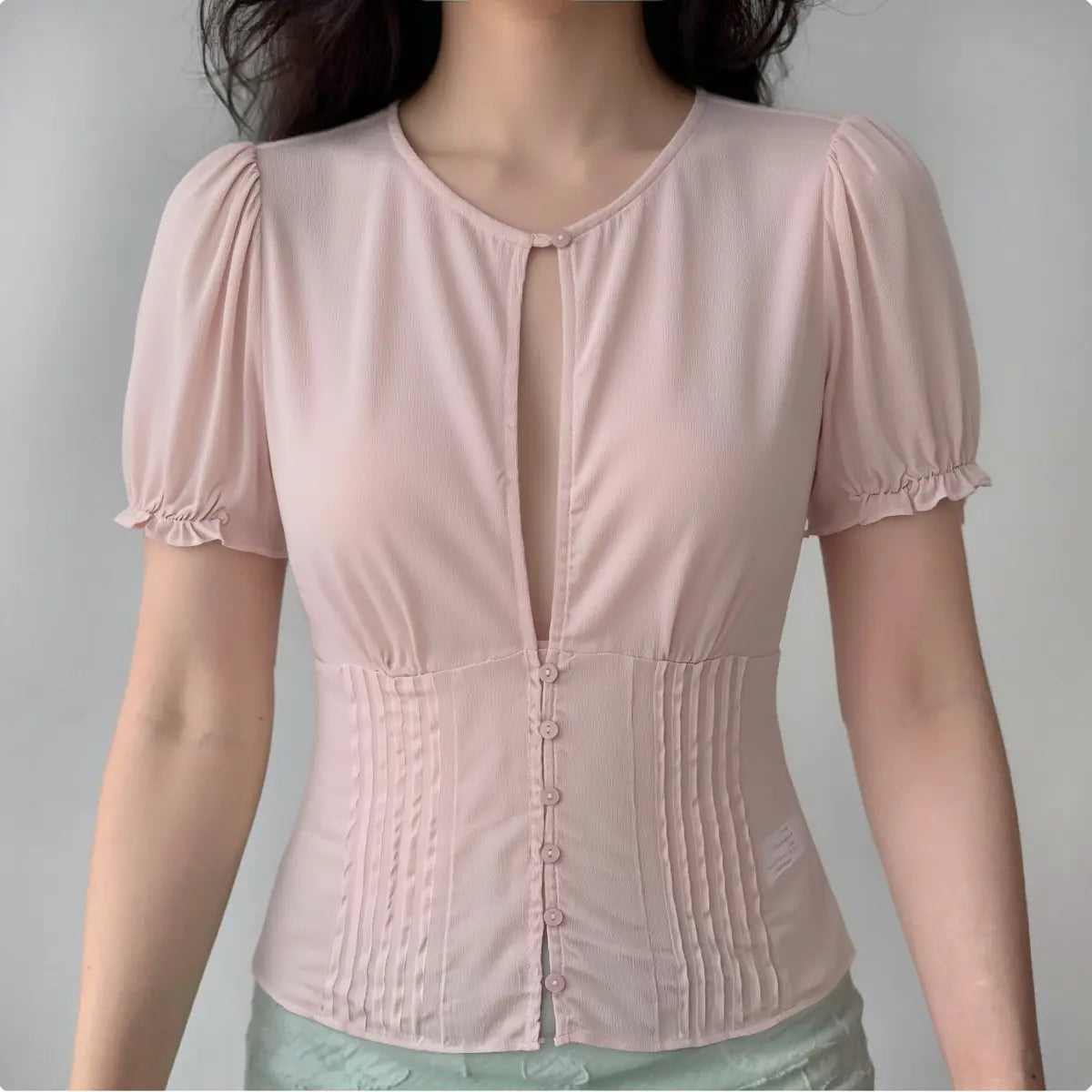 Model wearing light pink puff-sleeve blouse with keyhole neckline and pintuck waist, feminine vintage-inspired top