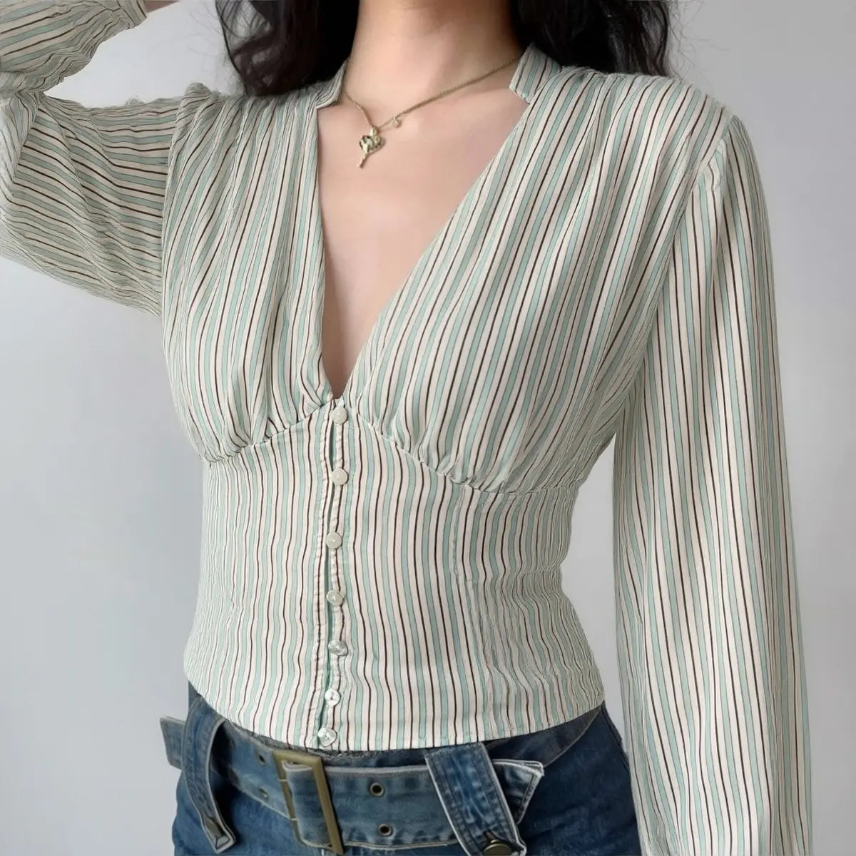 Model wearing light striped blouse with deep V-neck, button-down front, gathered bust detailing, and fitted cropped silhouette
