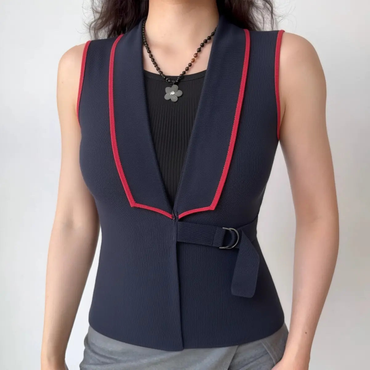 Model wearing navy knit vest with red contrast piping, buckle belt and tailored silhouette