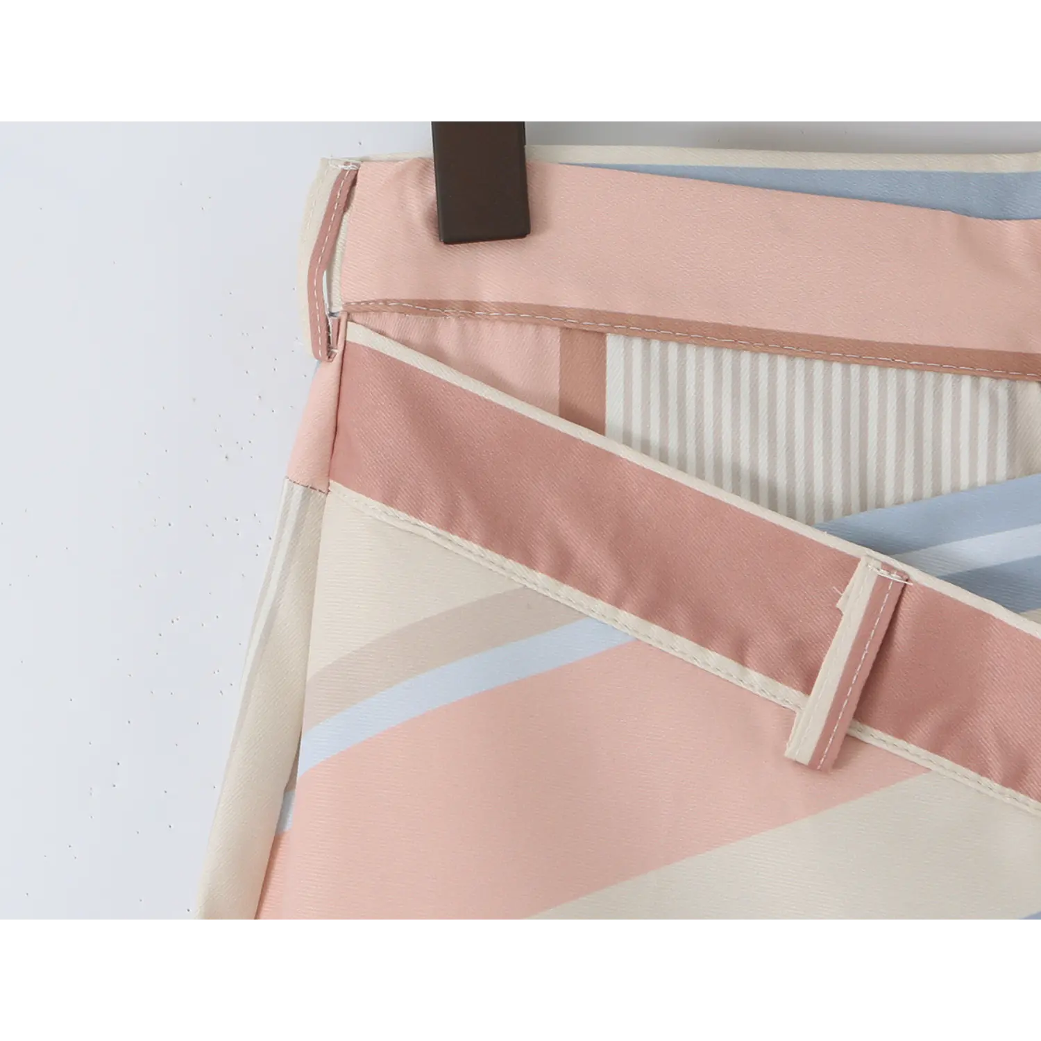 Macro shot of off-white four-hole button sewn on diagonal striped wrap overlay, uniform edge topstitching