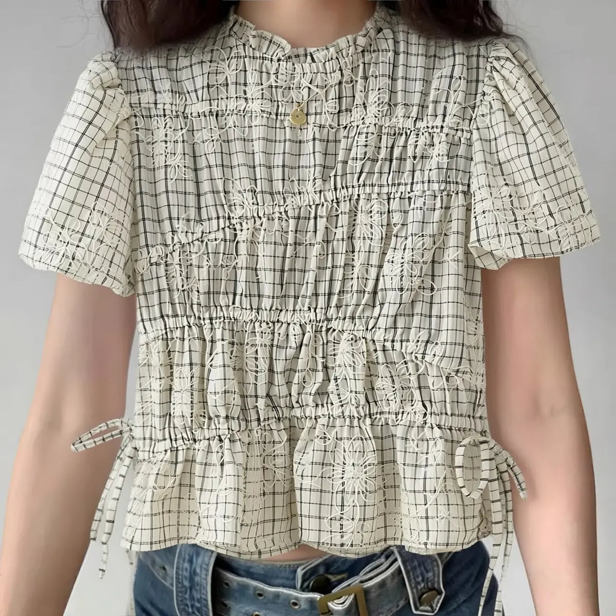 Model wearing off-white gingham blouse with floral embroidery and side drawstrings, vintage-inspired short-sleeve top