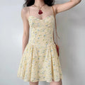 Model wearing pale yellow ditsy floral spaghetti-strap mini dress with corset-style bodice, romantic feminine summer dress