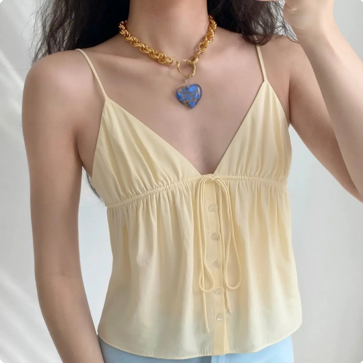 Model wearing pale yellow tie-front V-neck cami top with button detail, flowy casual cropped blouse
