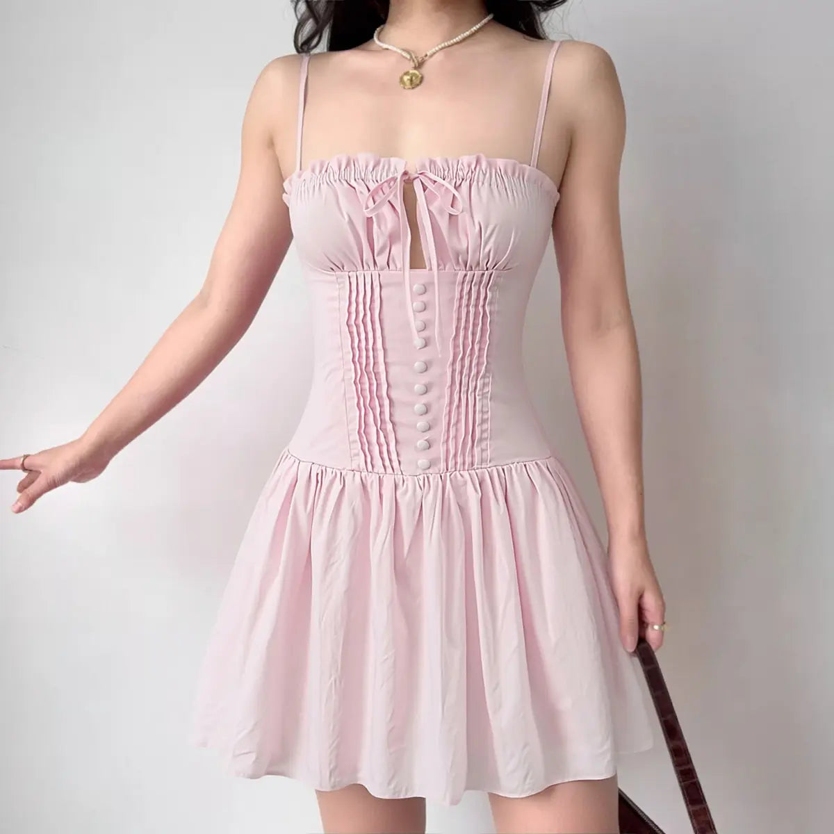Model wearing pink bow-front corset-style mini dress with button detail, romantic feminine party dress