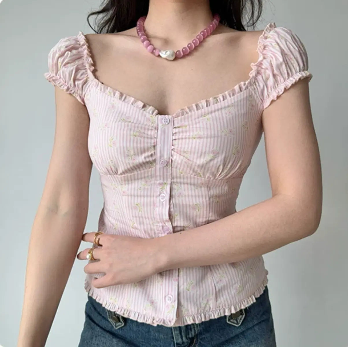 Model wearing pink floral gingham top with ruffled sweetheart neckline, cap sleeves and button-down front