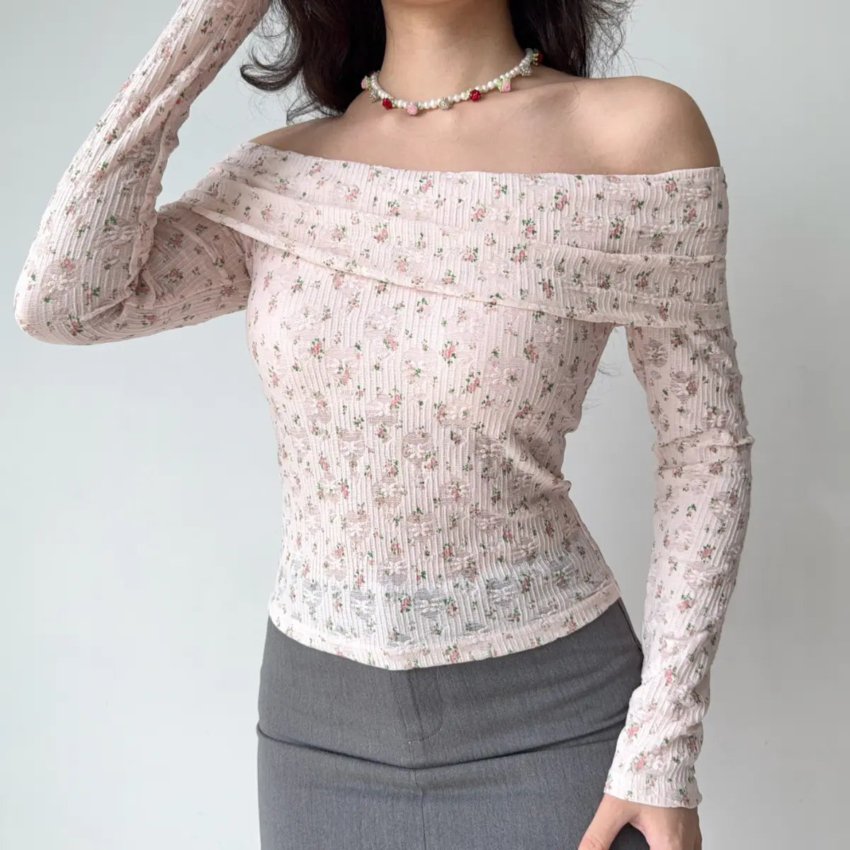 Model wearing pink floral-print off-the-shoulder top, raising arm to show sleeve length and fit, ribbed lace detail