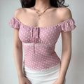 Model wearing pink-white polka-dot top styled as off-the-shoulder, with ruffled sleeves, lace trim and front tie detail